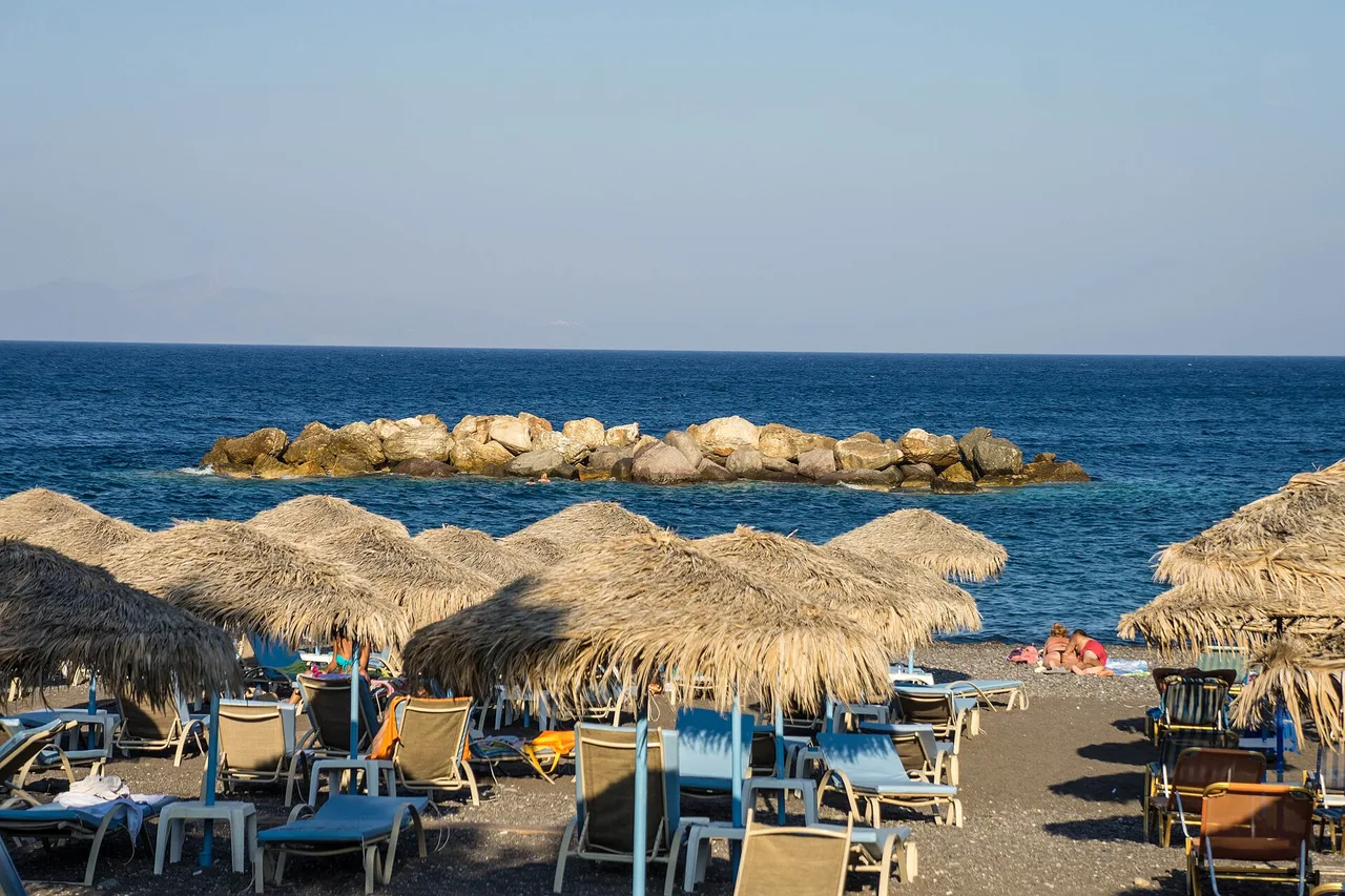 La plage de sable noir de Kamari, parasols de paille et transats face à la mer