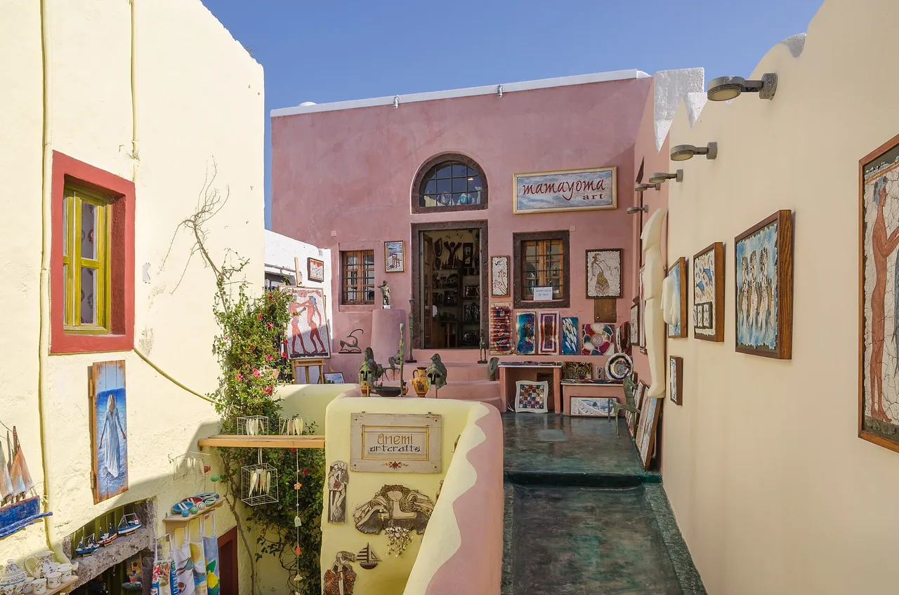 Une ruelle piétonne étroite d’Oia bordée de boutiques aux façades roses et jaunes