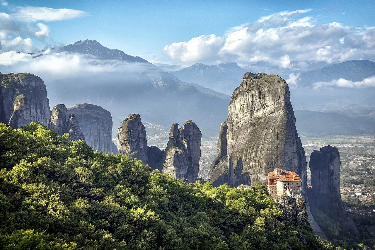 The rock pillars of Meteora emerging from the clouds at dawn, a monastery clinging to the stone
