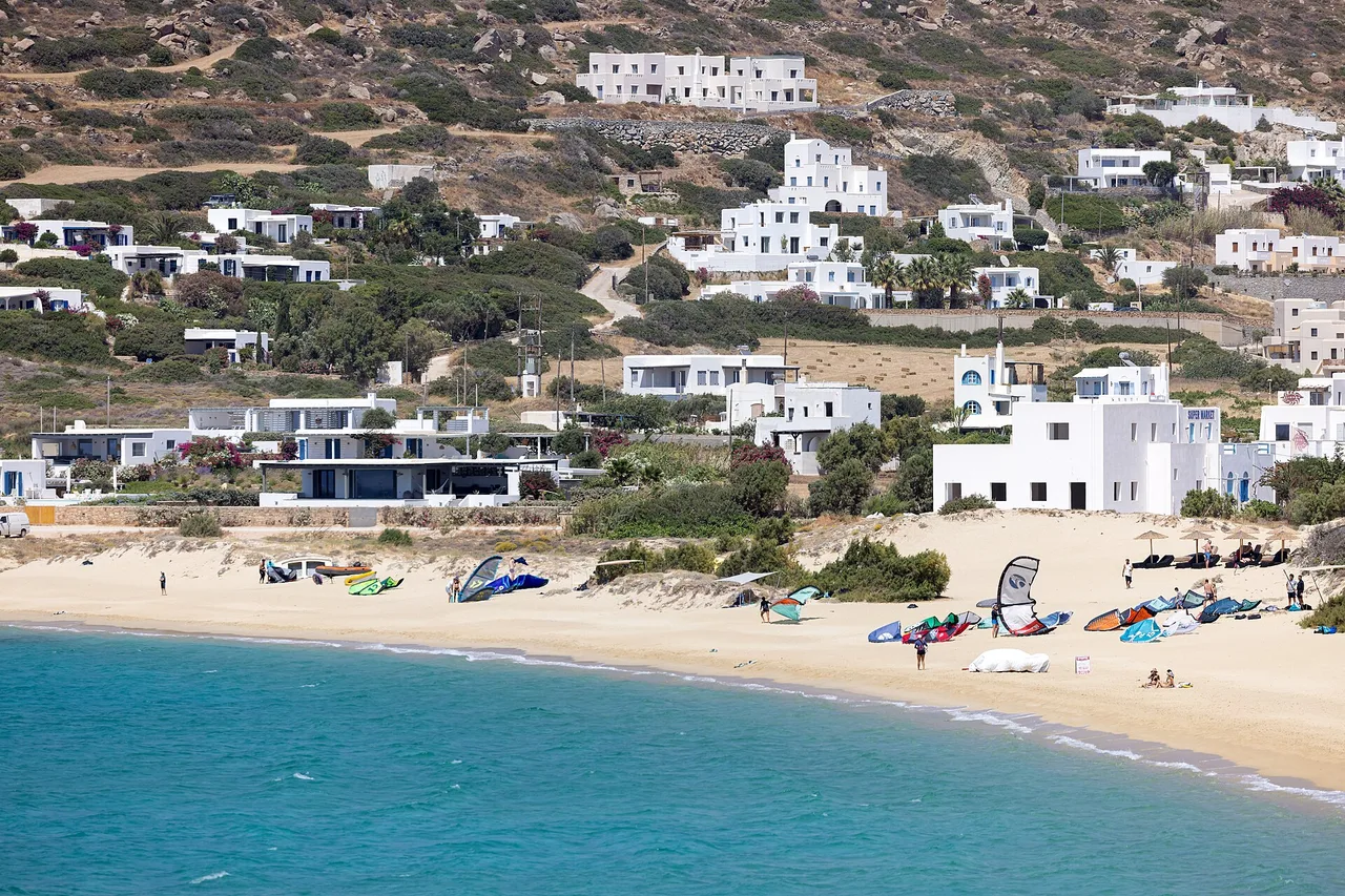A sandy beach on Naxos with turquoise water, white houses on the hill and sails laid on the sand