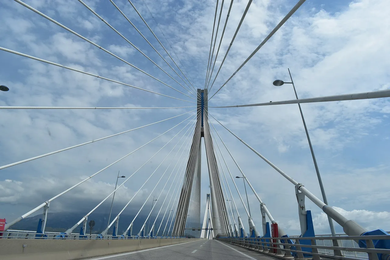 Vue depuis la chaussée du pont Rio–Antirrio sur un pylône d’où partent des haubans blancs en éventail, avec des garde-corps bleus