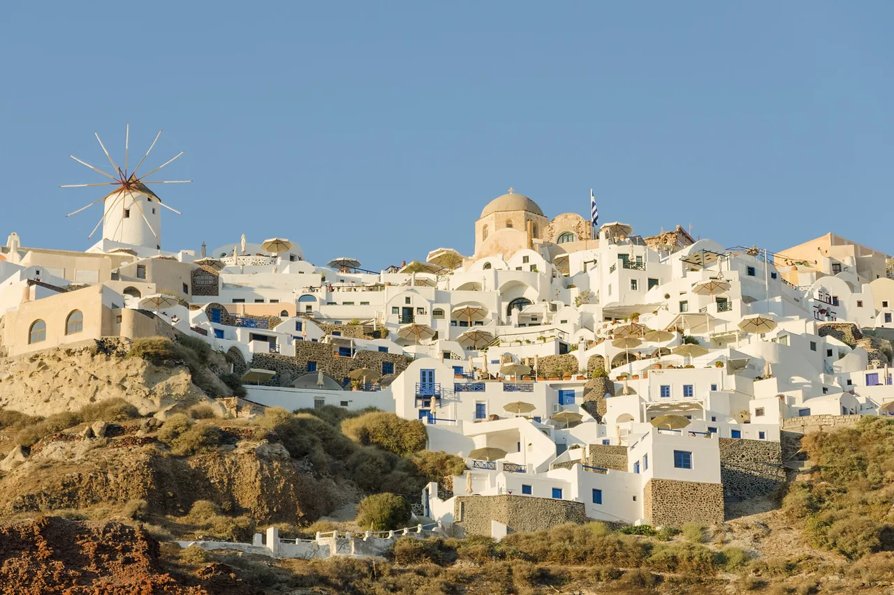 Il villaggio bianco di Oia sul pendio a Santorini, un mulino a vento a sinistra, le cupole delle chiese dietro e il cielo azzurro