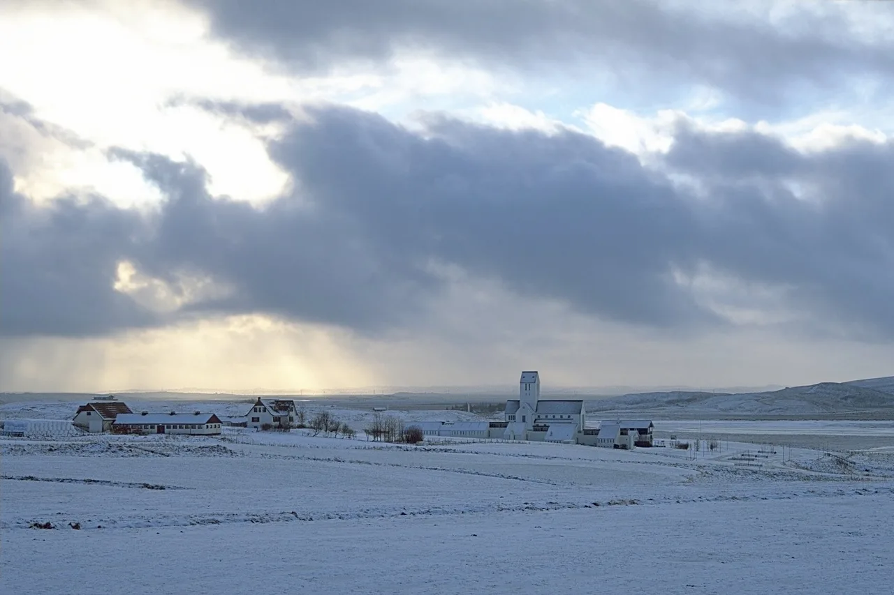 Spessa coltre di nuvole grigie squarciata da un raggio di luce su una pianura islandese innevata