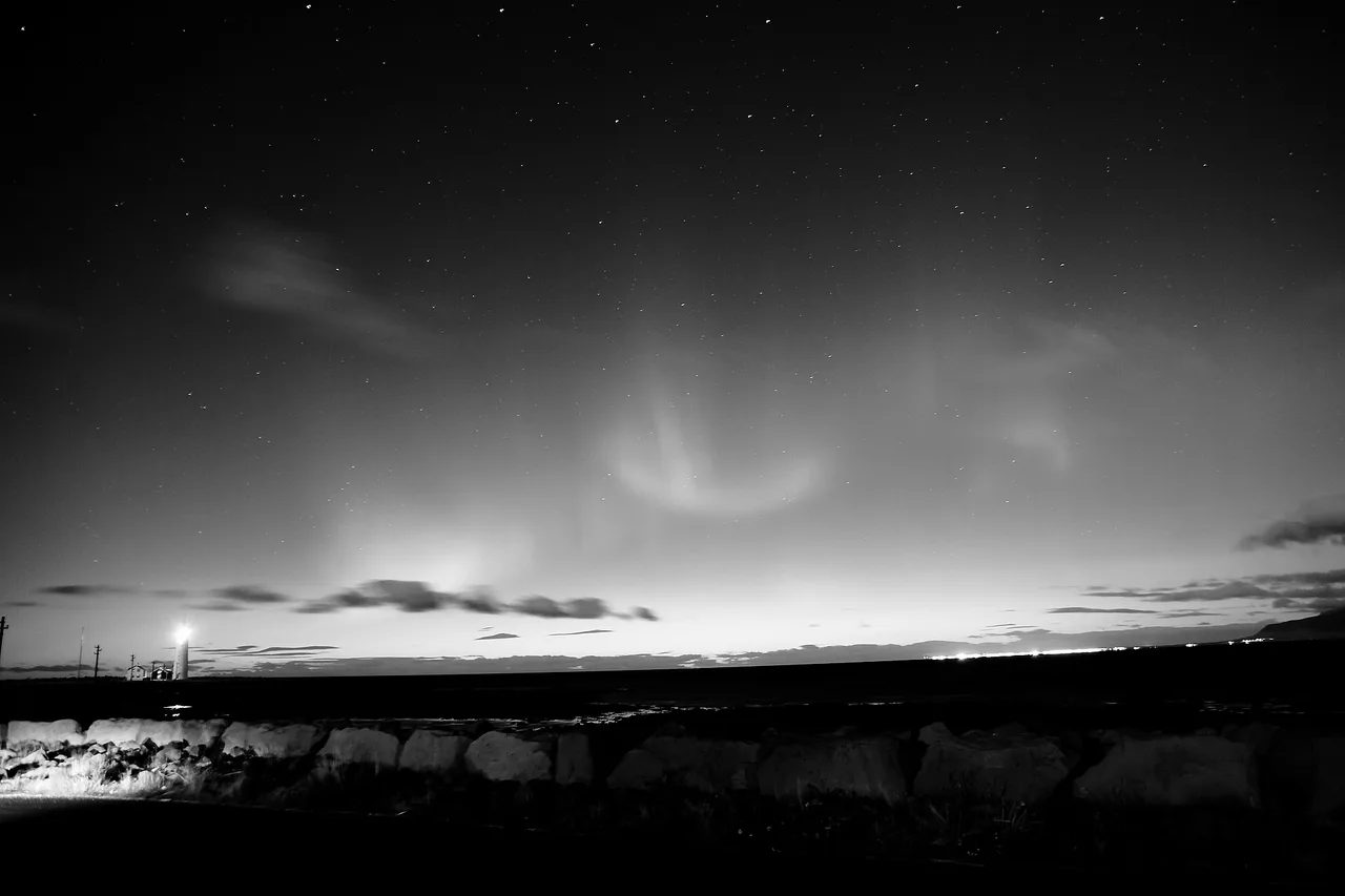 Aurora boreale bianca e grigia fotografata senza colore sopra un orizzonte scuro