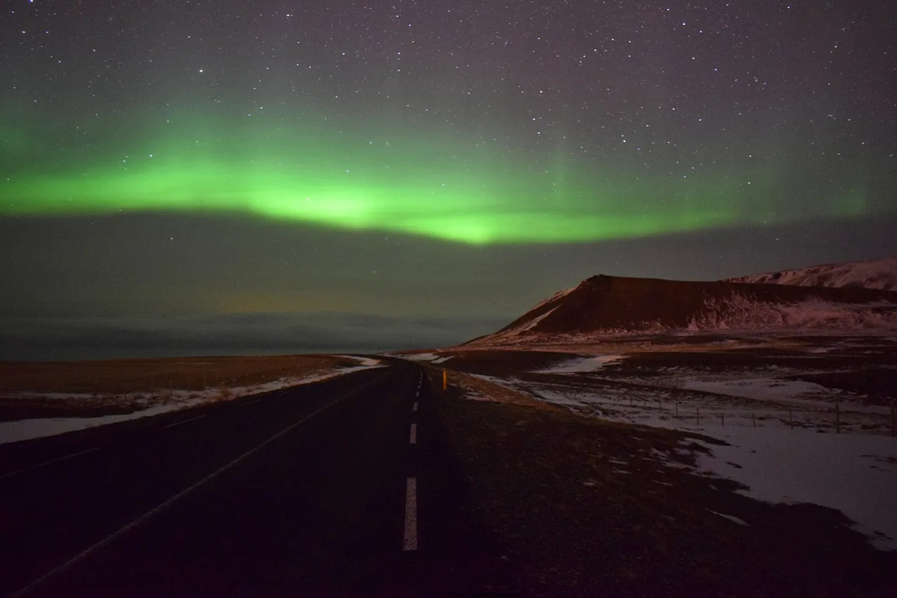 Strada islandese deserta di notte sotto una fascia verde di aurora boreale