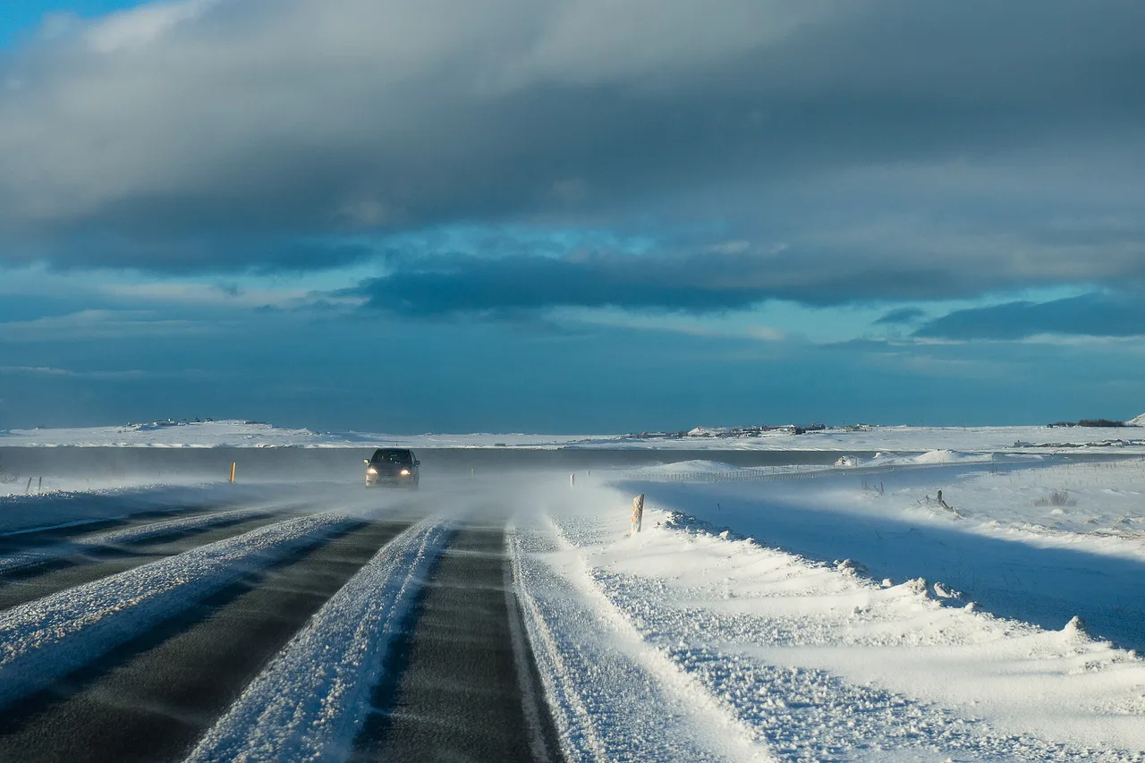 Vom Wind über eine isländische Straße getriebener Schnee, ein Auto in der Ferne