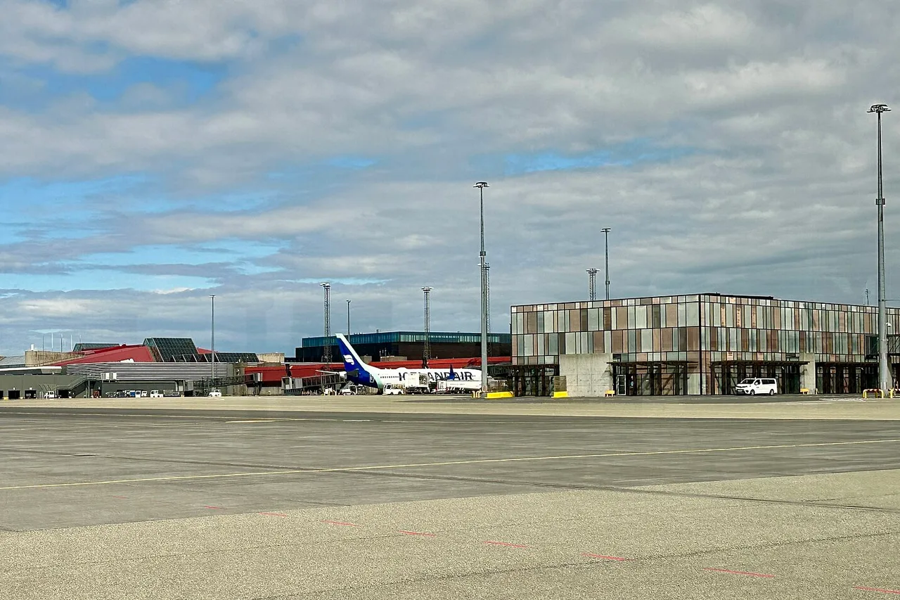 Das Terminalgebäude des Flughafens Keflavík mit Glasfassade in Kupfertönen, davor das Rollfeld und ein Verkehrsflugzeug am Gate