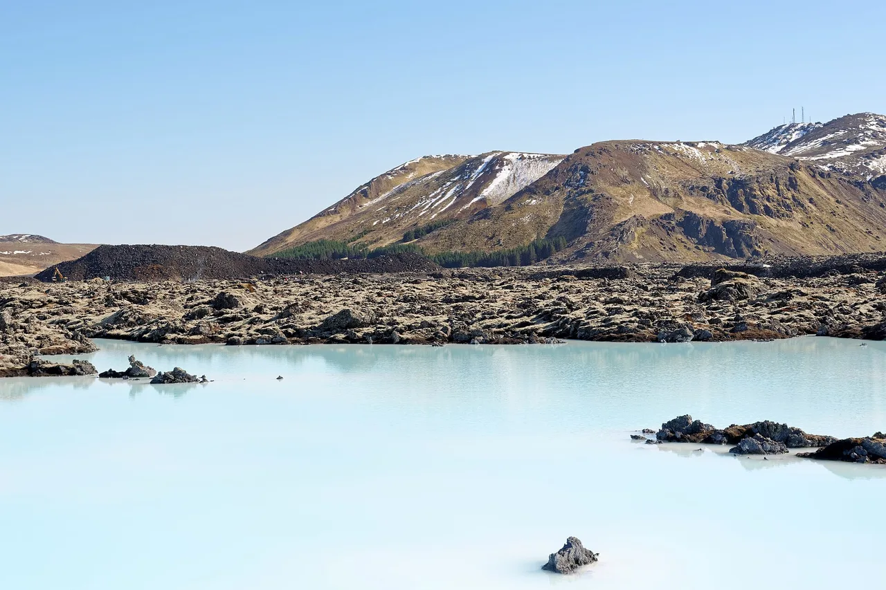 Das milchig hellblaue Wasser der Blue Lagoon vor schwarzen Lavafeldern, im Hintergrund der Berg Þorbjörn.