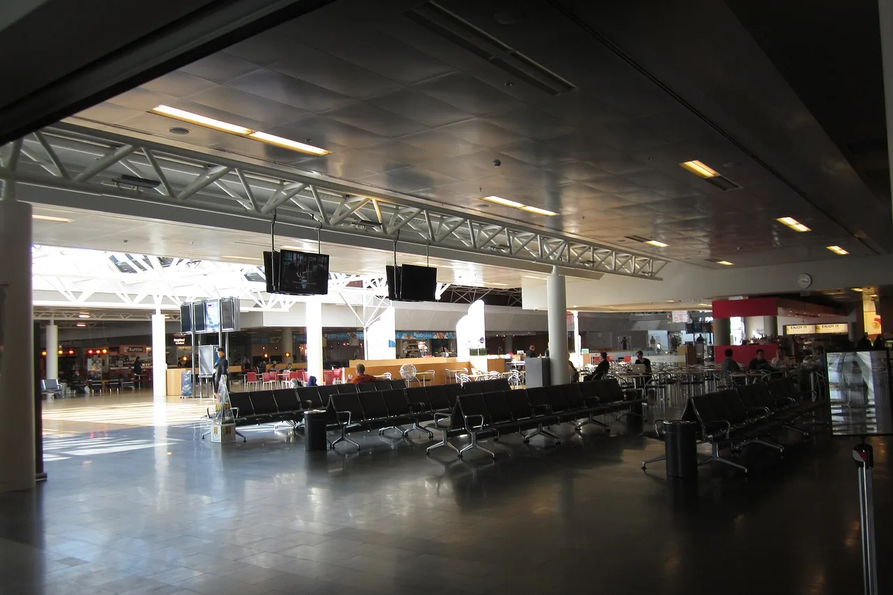 Grande salle d’attente du terminal de l’aéroport de Keflavík, rangées de sièges noirs, écrans d’information et restaurants au fond