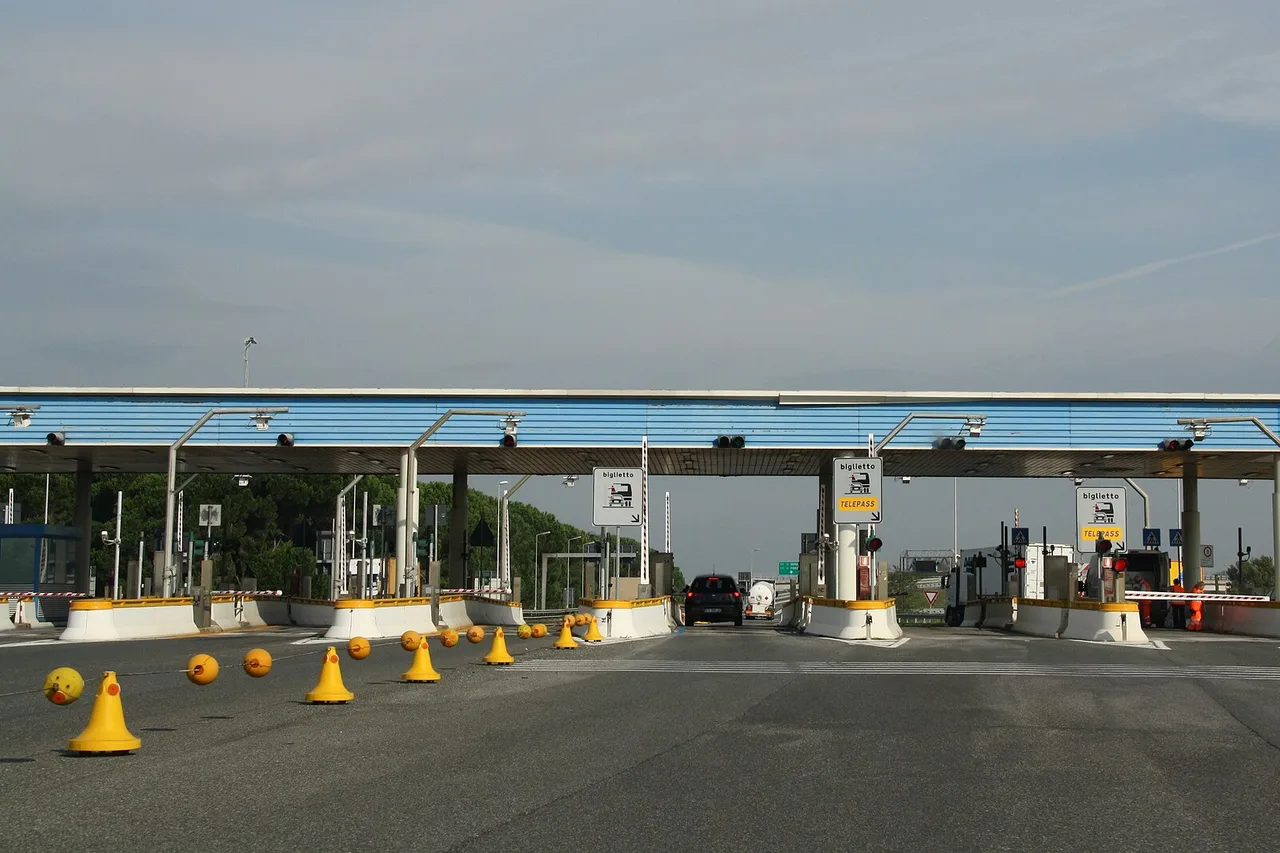 Une barrière de péage de l’autostrada A12 près de Livourne, sous un toit bleu, avec au-dessus d’une voie un panneau jaune « riservata clienti Telepass »