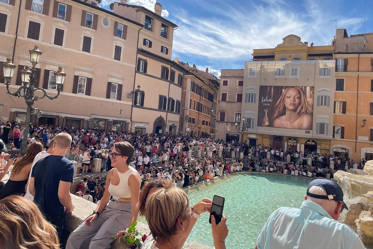 Viele Menschen sitzen und stehen am Rand des Trevi-Brunnens in Rom, im Hintergrund Häuser in Ockertönen