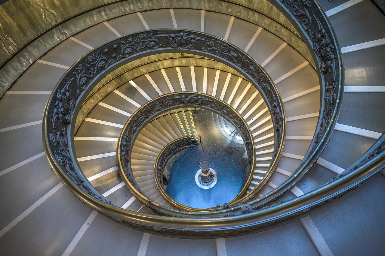 Eine Wendeltreppe mit schmiedeeisernem Geländer in den Vatikanischen Museen, die Spiralen laufen auf einen hellen Punkt in der Mitte zu