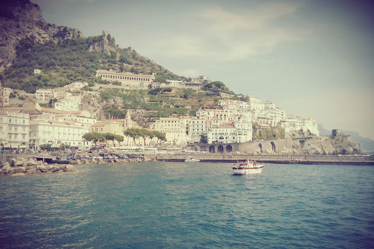Amalfi seen from the ferry dock: pale houses on a slope above the harbour and a boat on the water