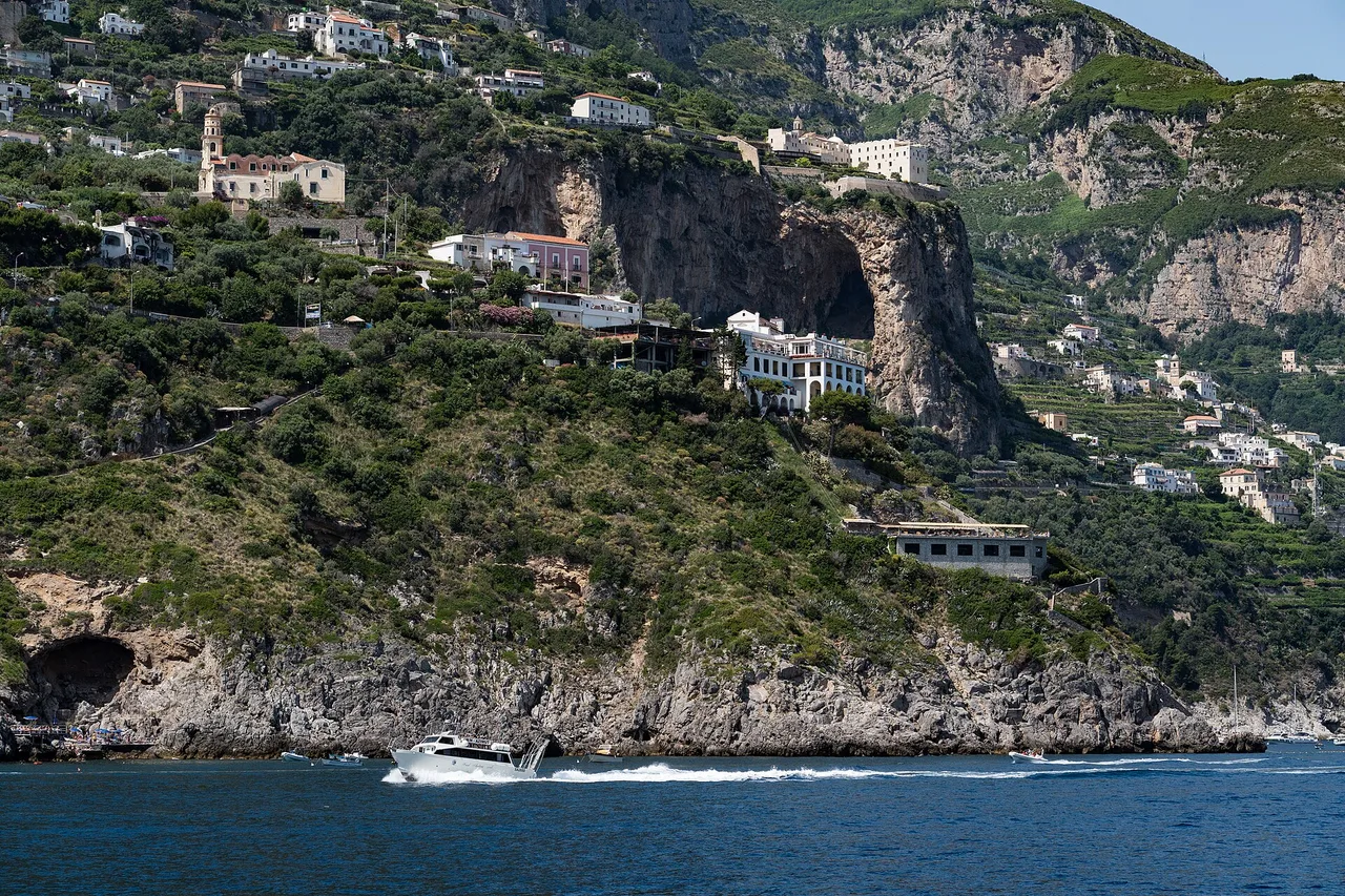 View from the water of the steep coast between Amalfi and Positano: a rock face, houses clinging to the slope and a small boat