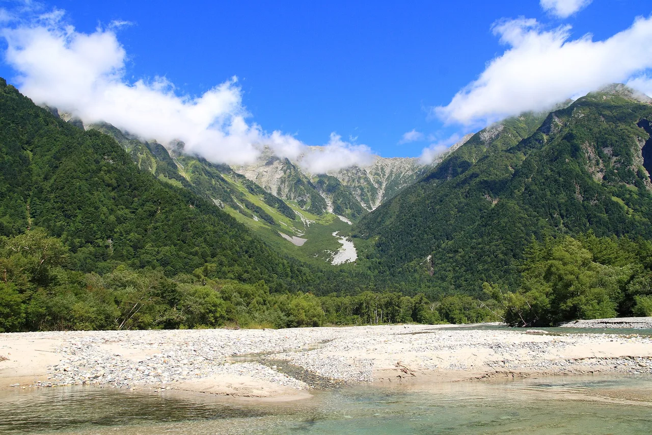 Fond de vallée de Kamikochi dans les Alpes japonaises : lit de galets, rivière, versants boisés et nuages sur les sommets
