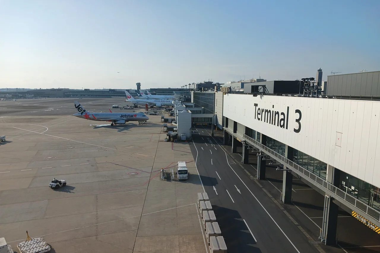 Terminal 3 de l’aéroport de Narita, avec le tarmac, un avion Jetstar et la façade du bâtiment sous un ciel dégagé