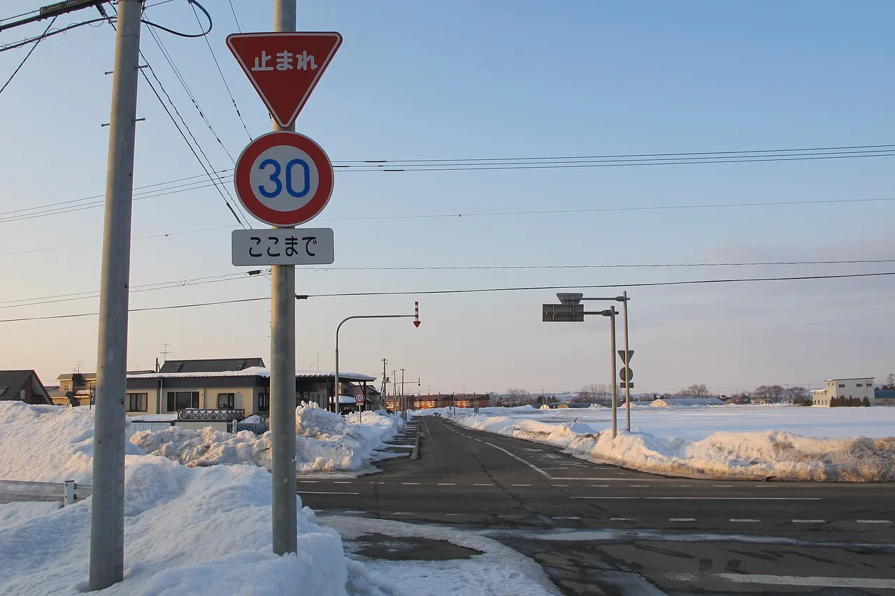 Un incrocio innevato a Hokkaido con il triangolo rosso « 止まれ » (stop) e un cartello di limite a 30 km/h