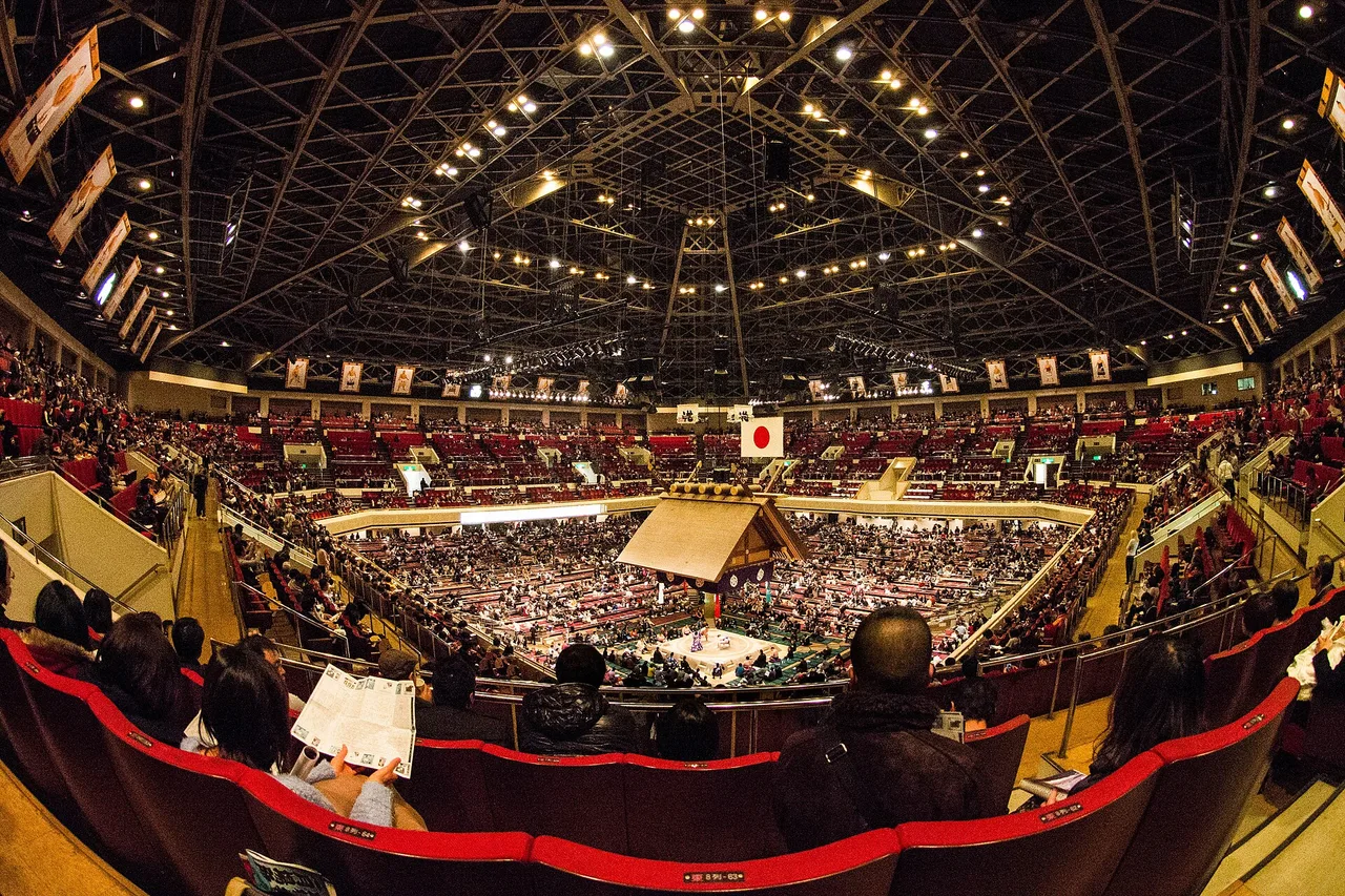 L’intérieur du Ryogoku Kokugikan à Tokyo pendant un tournoi de sumo, gradins autour de l’aire de combat sous la charpente