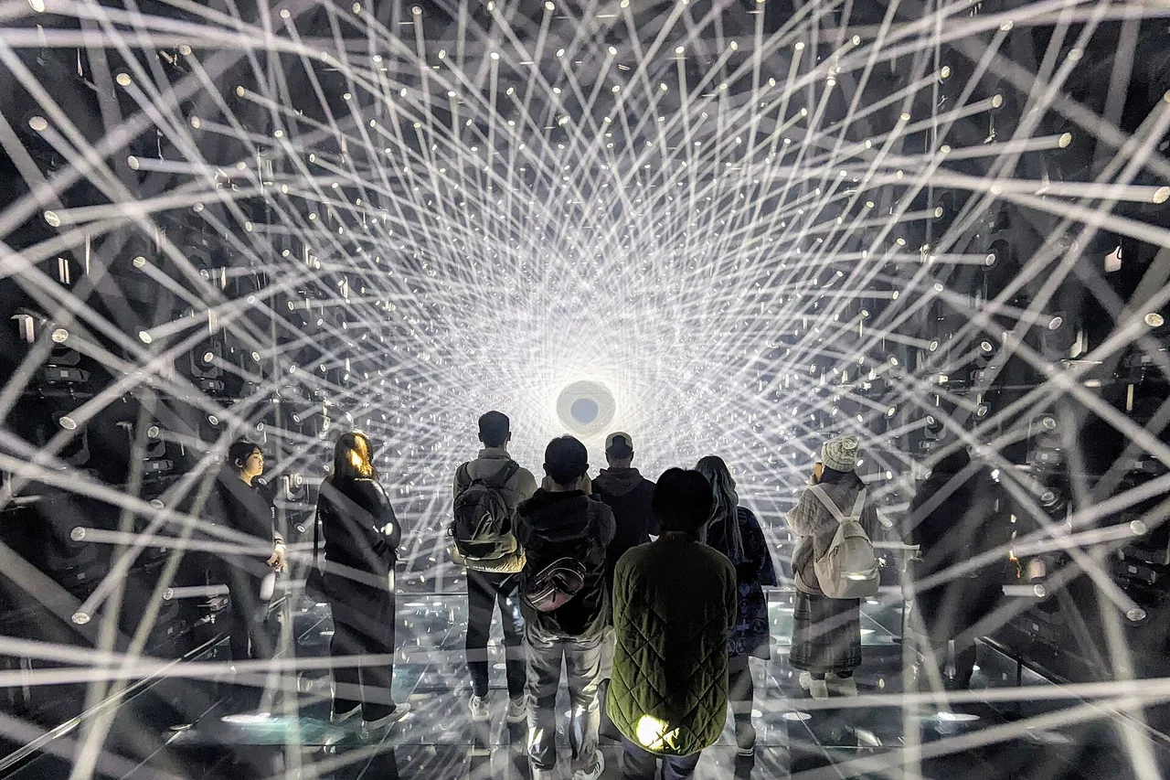 Visiteurs dans une salle de miroirs et de lignes lumineuses à teamLab Borderless, à Azabudai Hills