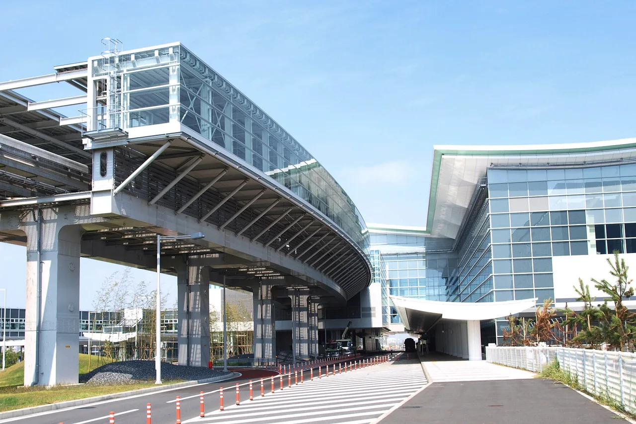Internationales Terminal des Flughafens Haneda mit geschwungenem Glasdach, Hochbahn und Vorfahrt bei klarem Himmel