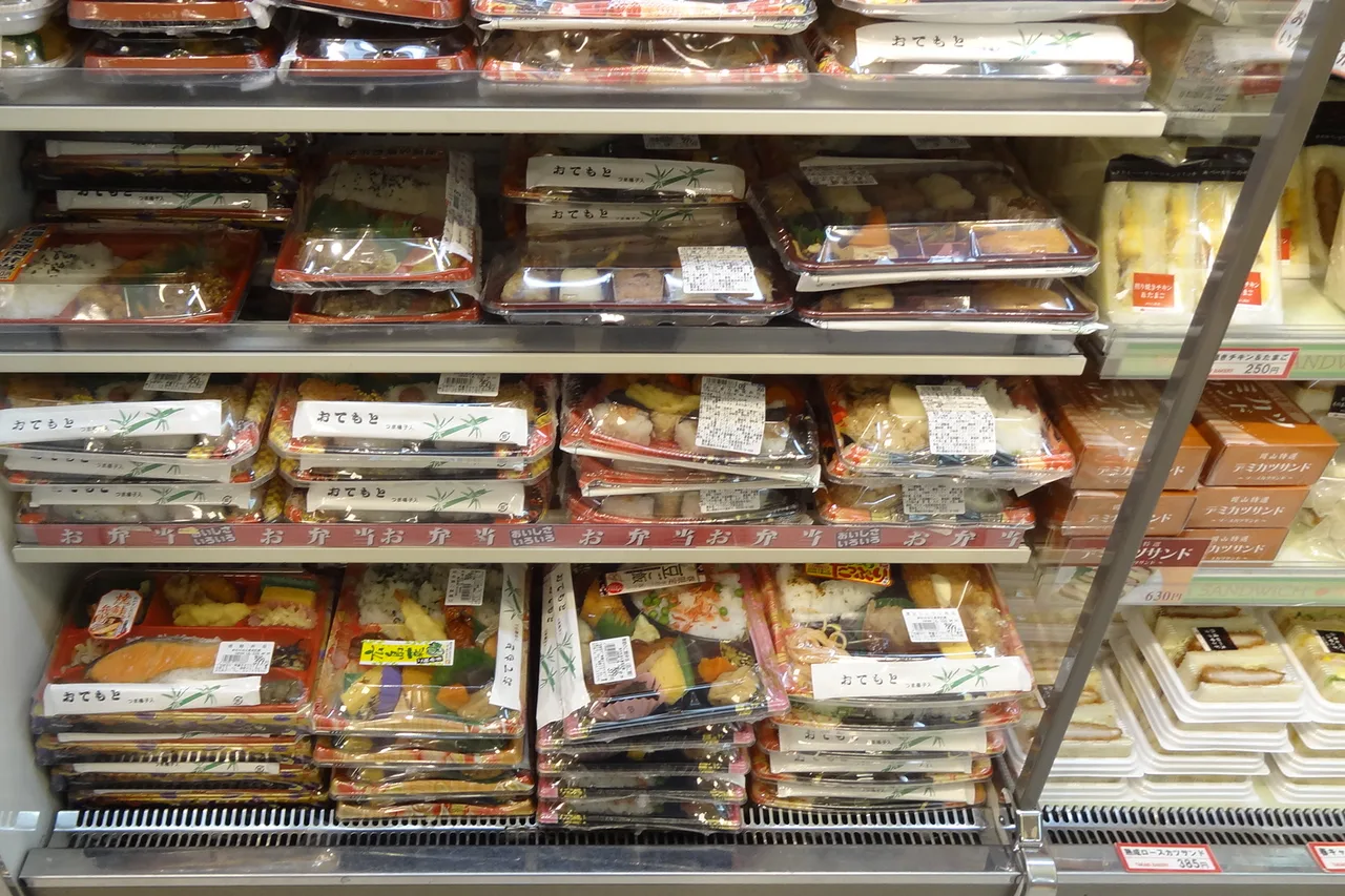 Scaffale di bentō e piatti pronti in un minimarket giapponese, cartellini dei prezzi visibili