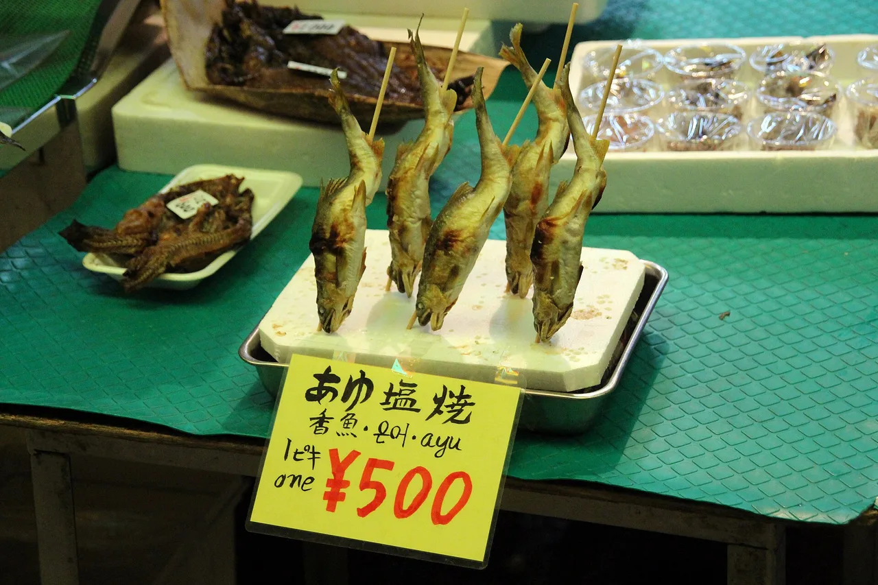 Pesci grigliati su una bancarella del mercato Nishiki di Kyoto con un cartellino giallo da 500 yen