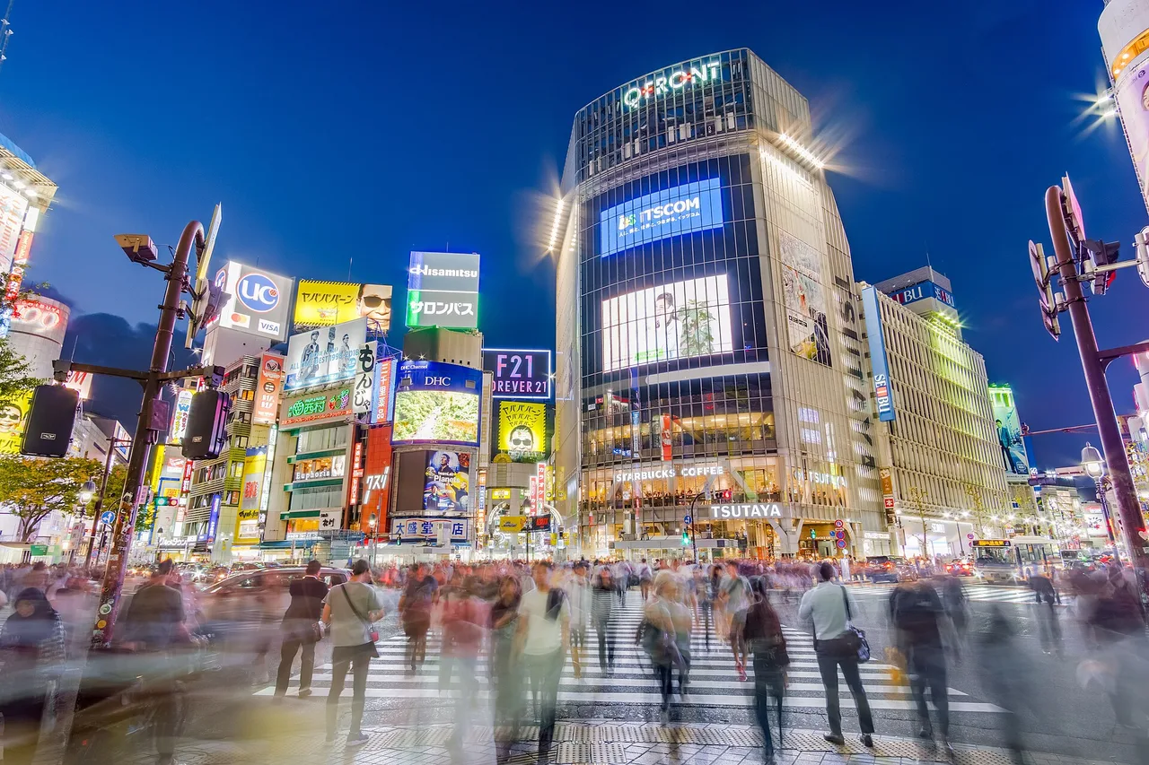 L’incrocio di Shibuya a Tokyo all’ora blu, folla in movimento e facciate di insegne al neon