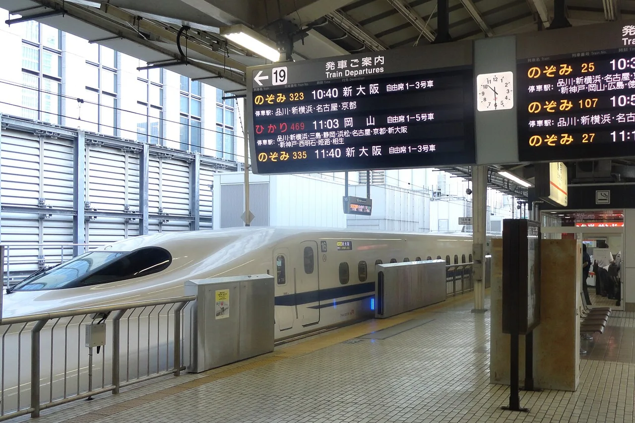 Tabellone delle partenze con i treni Nozomi accanto a un convoglio nella stazione di Tokyo