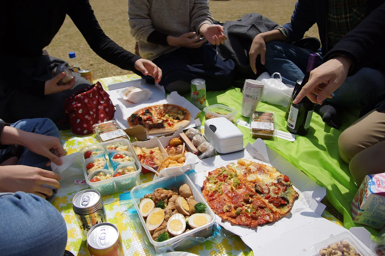 Comida de hanami dispuesta sobre una lona, platos compartidos y bebidas, en un parque japonés