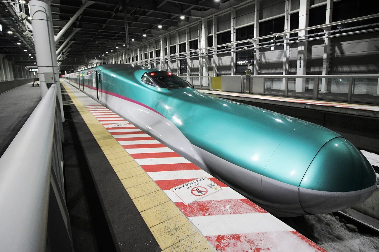 A green E5 series Shinkansen train at a platform under a snow-covered canopy