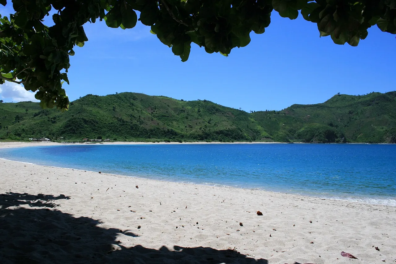 Hufeisenförmige Bucht mit weißem Sand, umgeben von grünen Hügeln, Süd-Lombok