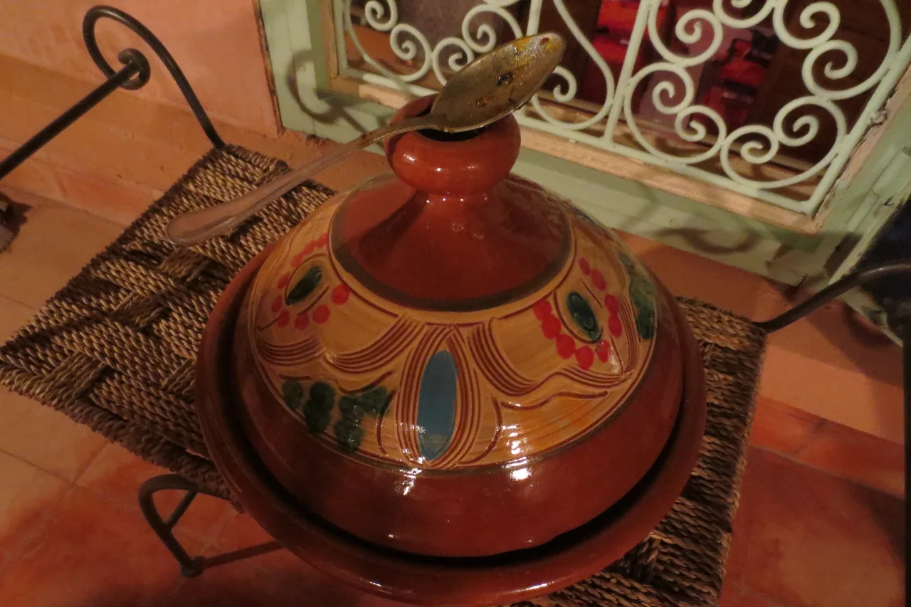 Un tajine en terre cuite fermé, posé sur son support en fer forgé