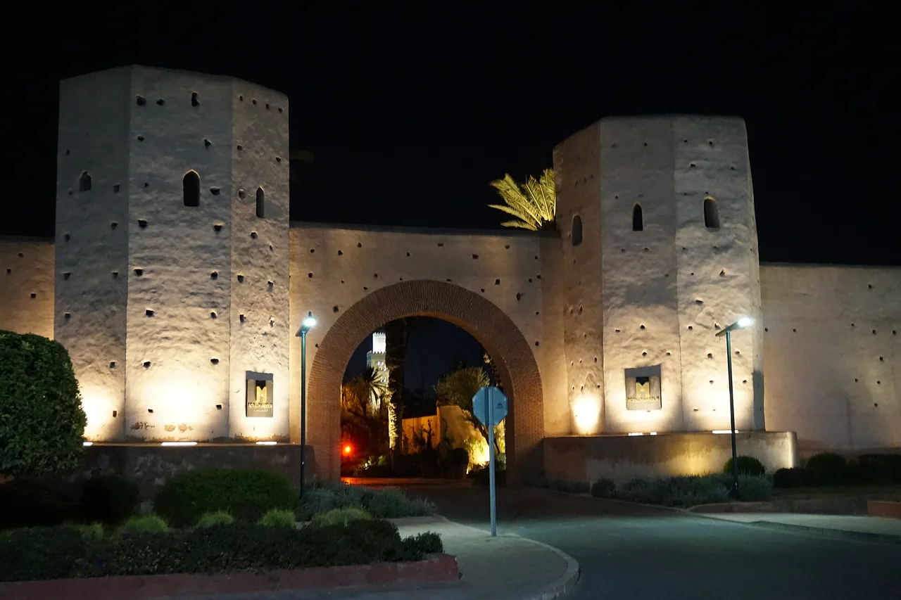 Una puerta de la muralla de Marrakech iluminada de noche, con la carretera y la rotonda delante