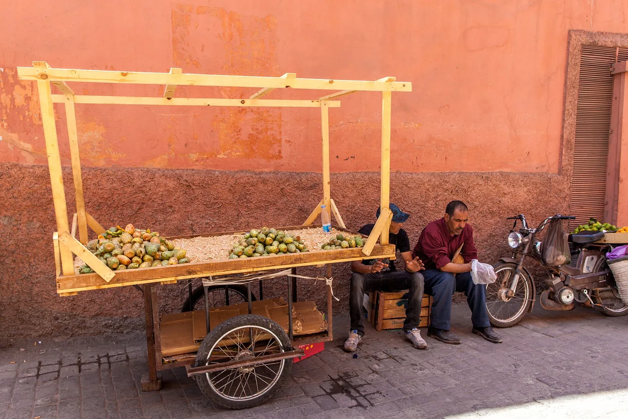 Una carreta de fruta y un ciclomotor apoyados en un muro ocre en un callejón de la medina de Marrakech