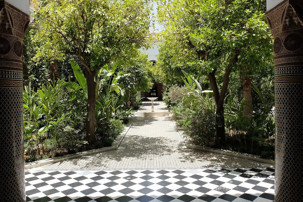 El jardín interior de una gran casa de la medina de Marrakech, con paseo enlosado en damero y árboles sobre el patio