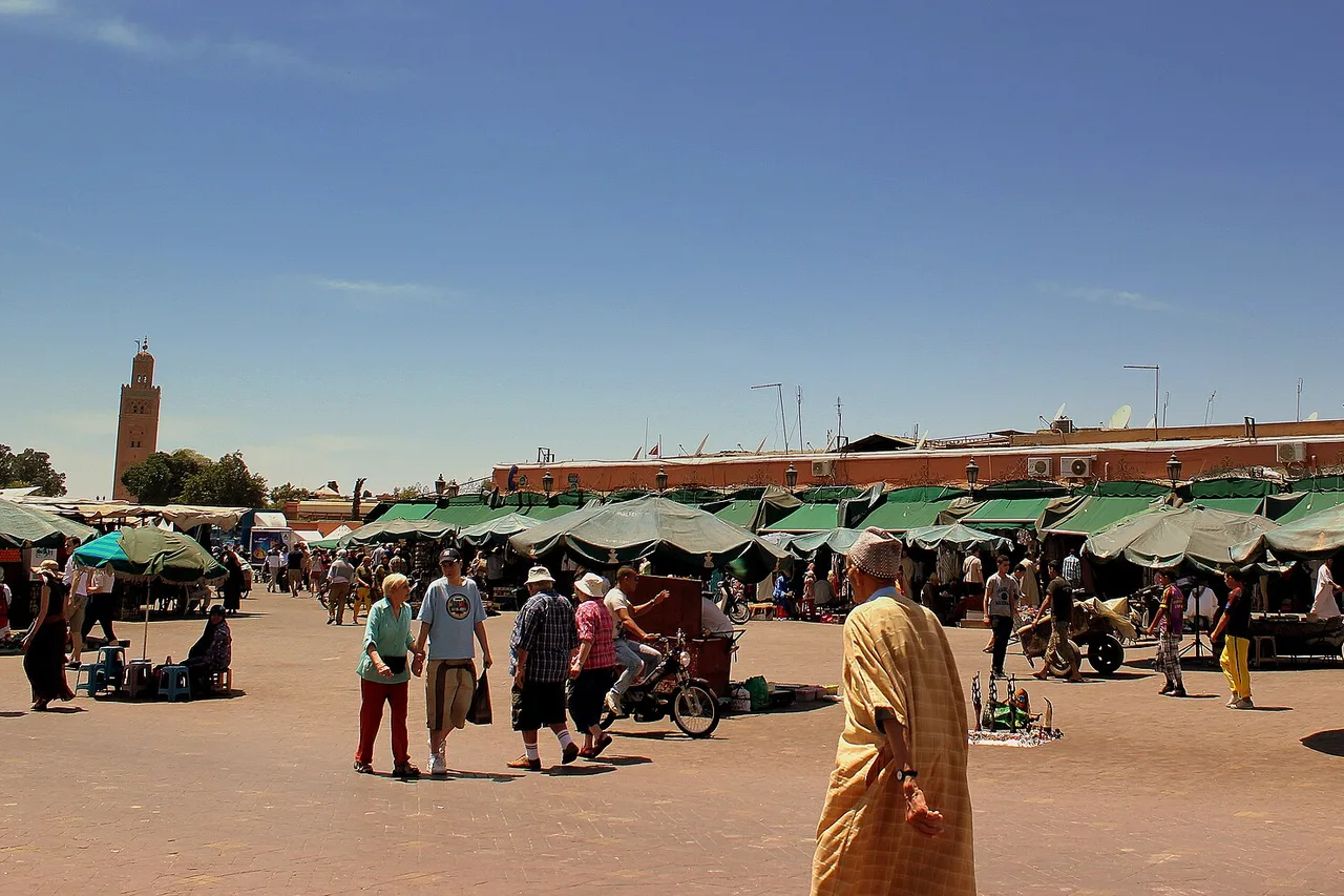 Jemaa el-Fna square in Marrakech in full daylight, without a scrap of shade, its parasols and the Koutoubia minaret in the distance