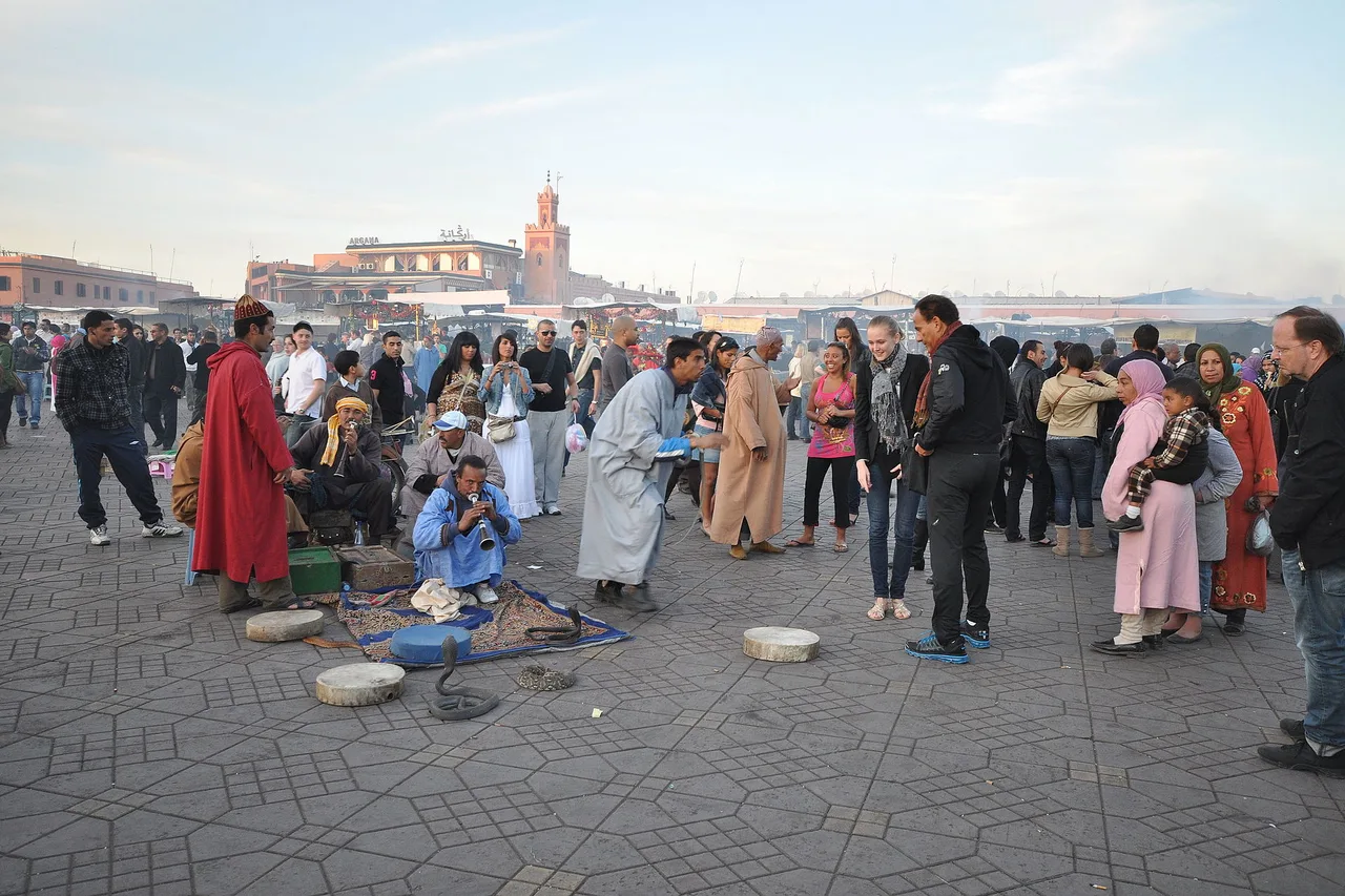 La folla di giorno sulla piazza Jemaa el-Fna, attorno ai cerchi di musicisti e domatori di animali