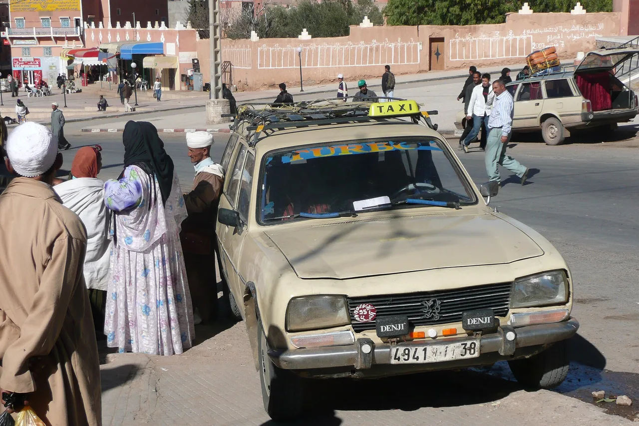 Un petit taxi beige a Marrakech, con passeggeri che trattano al finestrino sul ciglio della strada