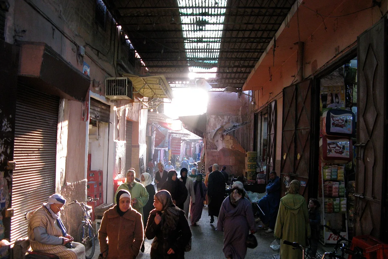 Un vicolo coperto del souk di Marrakech, illuminato da lucernari, con abitanti seduti davanti alle botteghe