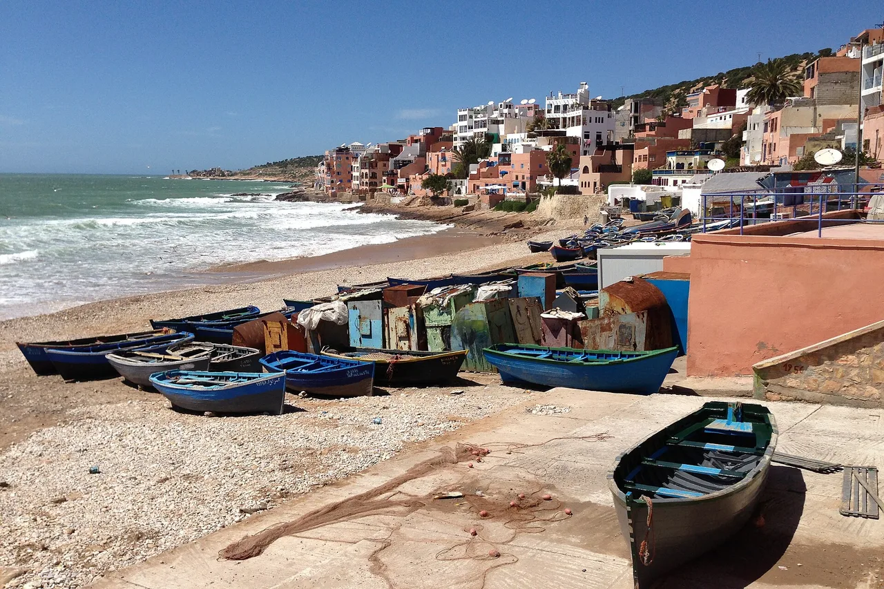 Blue fishing boats pulled up on Taghazout beach, in front of the village houses stacked on the slope