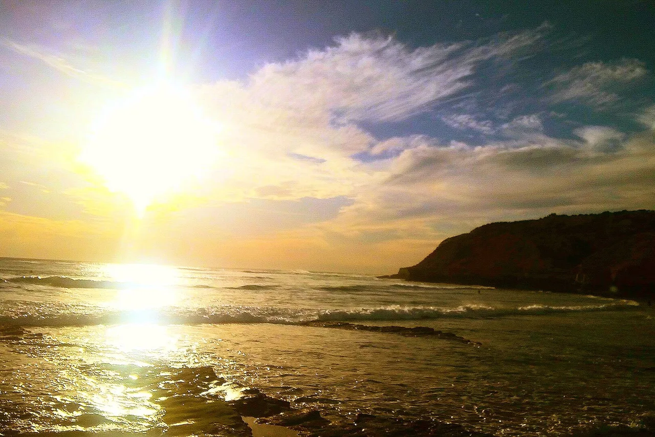 The sun setting behind a rocky headland on the Taghazout coast, with swell unrolling in long lines