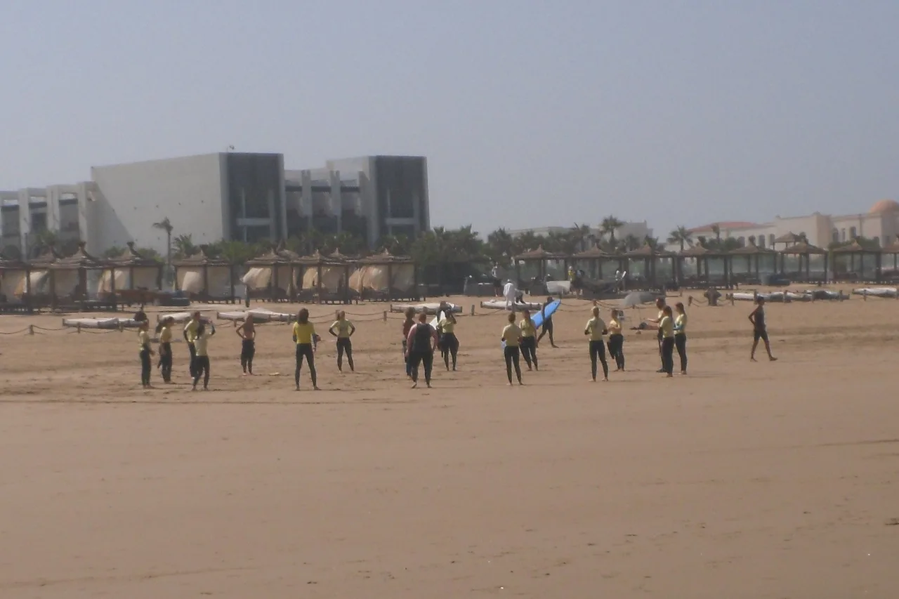 A group surf lesson lined up on the sand at Agadir, boards down, before going in