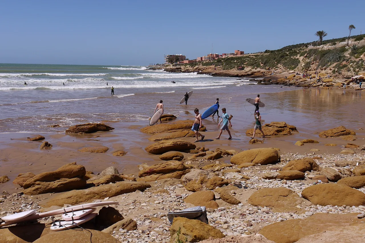 Surfers crossing the rock shelf at Taghazout, boards under their arms, on their way to the peak