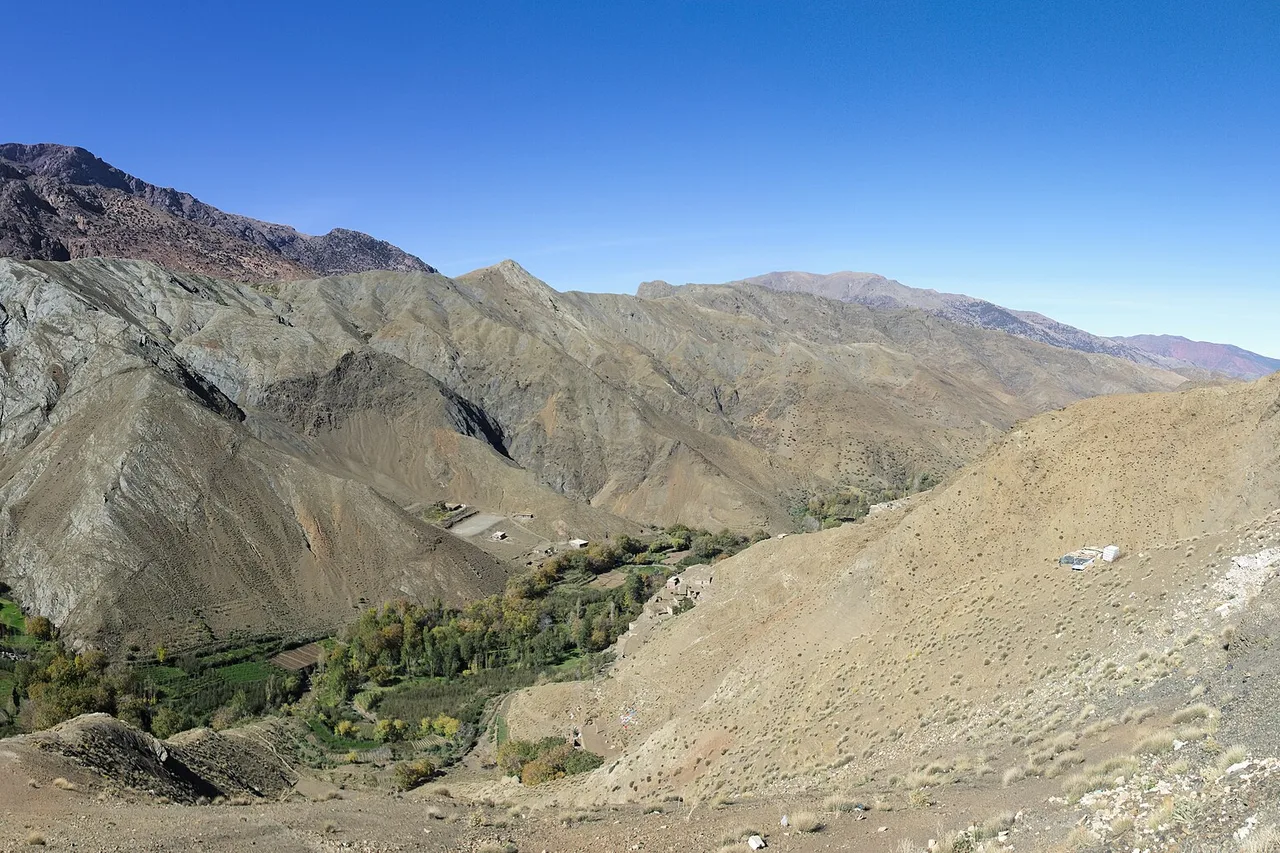 Valle del Alto Atlas con laderas áridas, una franja verde de huertos y un pequeño pueblo bajo un cielo sin nubes