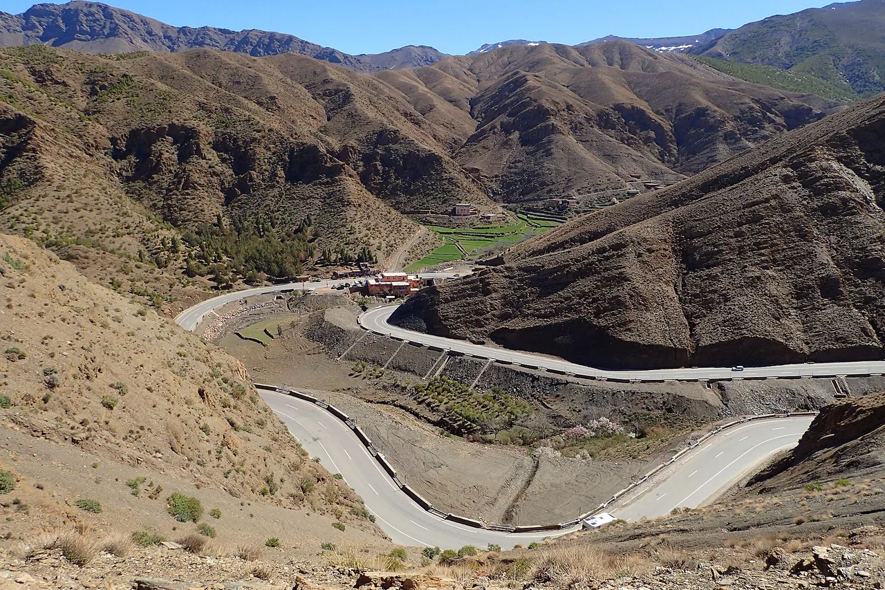 Una carretera de curvas cerradas baja por una ladera árida y rocosa cerca del puerto del Tizi n’Tichka, con manchas verdes en el fondo del valle