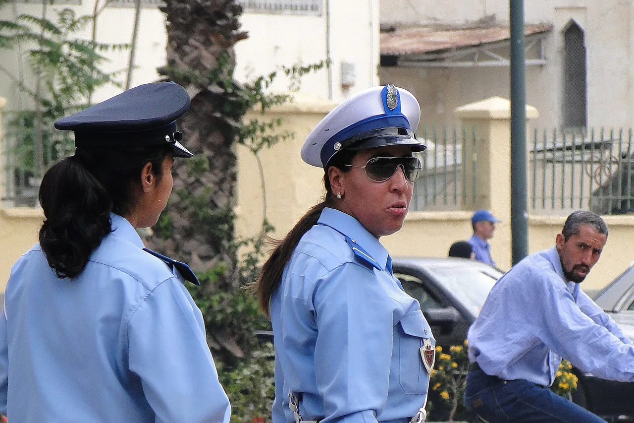 Dos agentes de tráfico mujeres con uniforme azul claro están en el borde de una calle de Meknes mientras un hombre pasa en bicicleta a su lado