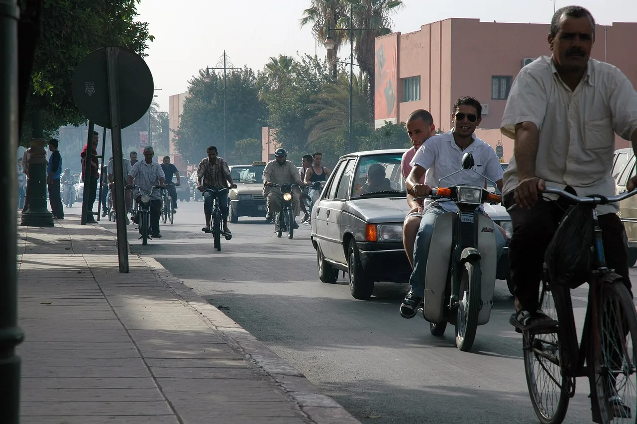 Una calle de Marrakech con motocicletas, ciclistas y un coche blanco antiguo en medio de un tráfico denso
