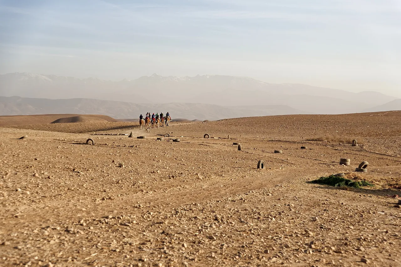 Le désert de pierre d’Agafay près de Marrakech, avec une petite caravane au loin et les sommets brumeux du Haut Atlas à l’arrière-plan