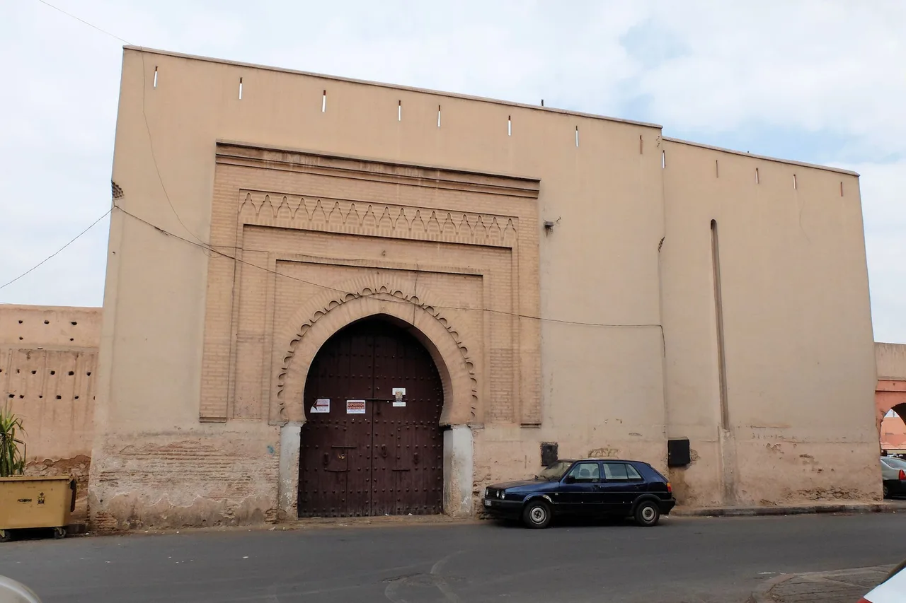 Alto muro ocra con un grande portale ad arco acuto dai battenti in legno scuro, Bab Doukkala, medina di Marrakech, un’auto parcheggiata davanti