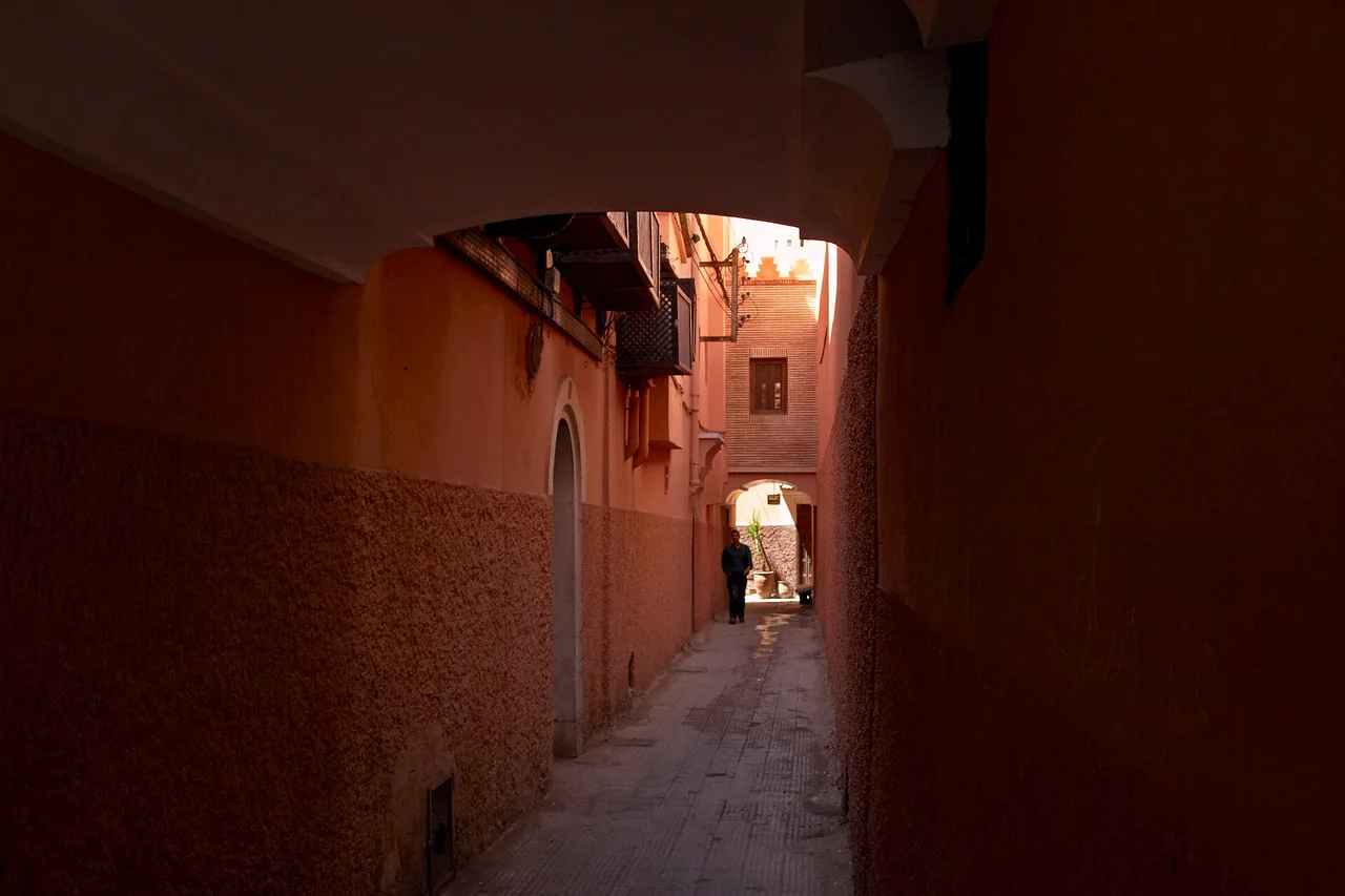 Stretto vicolo dai muri rosa e ocra nella medina di Marrakech, vicino a Bab Doukkala, un passante in controluce in fondo